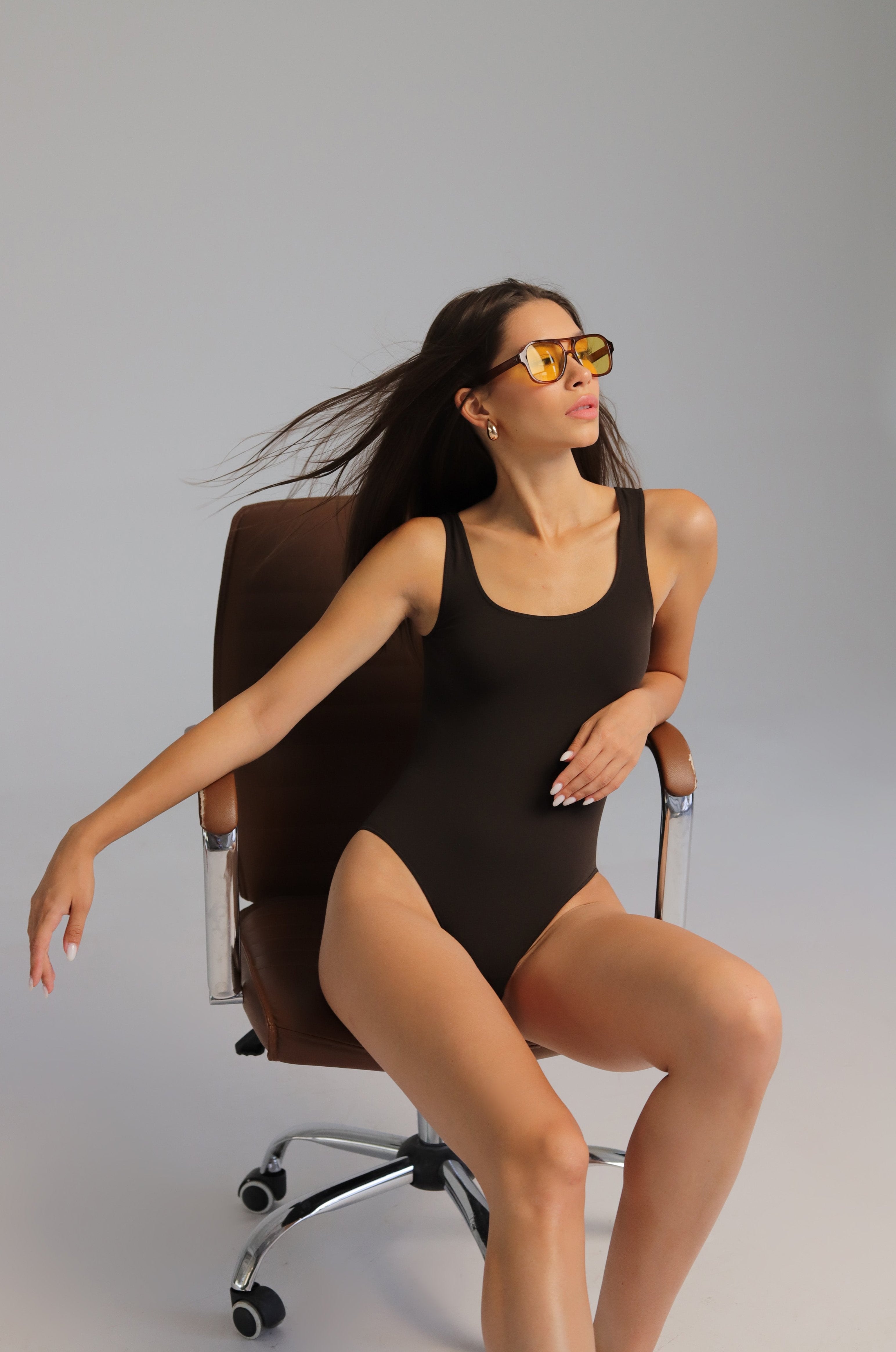 A wide strap bodysuit in brown color with a round neckline and three metal hooks at the bottom.